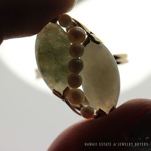 Backlit reverse view of the ring's two jade stones and central pearl row.