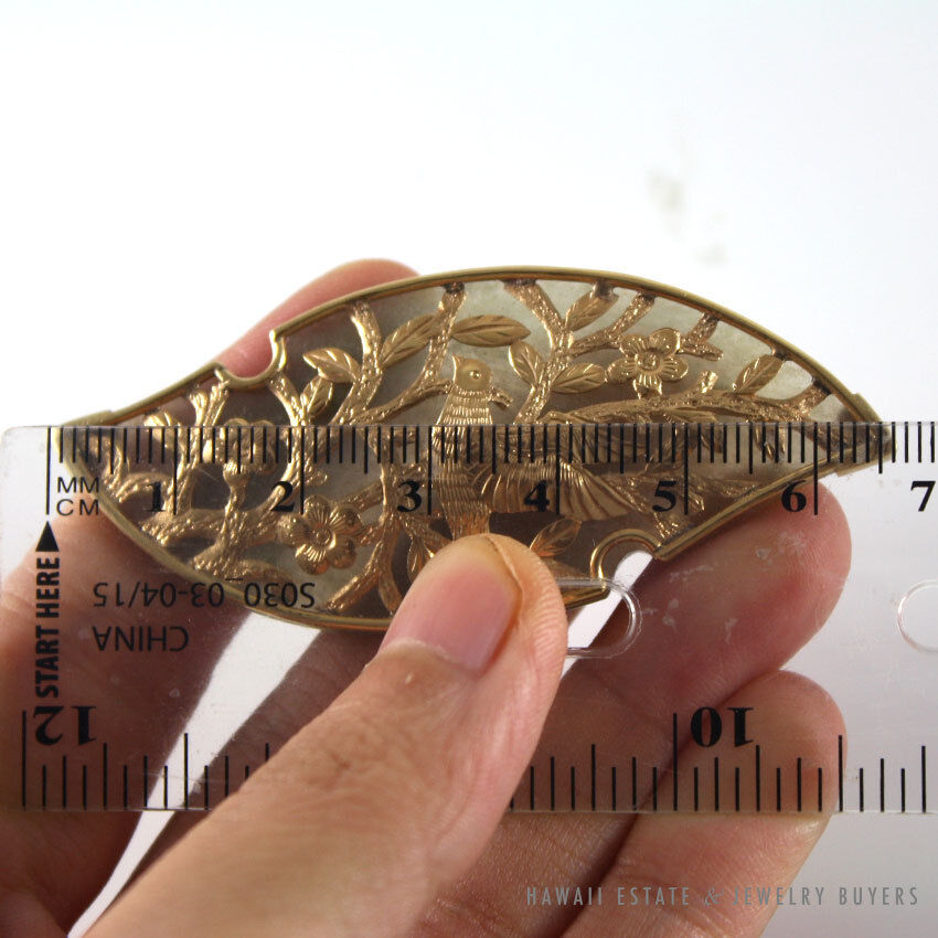 Bird-and-flower brooch shown across a metric ruler.