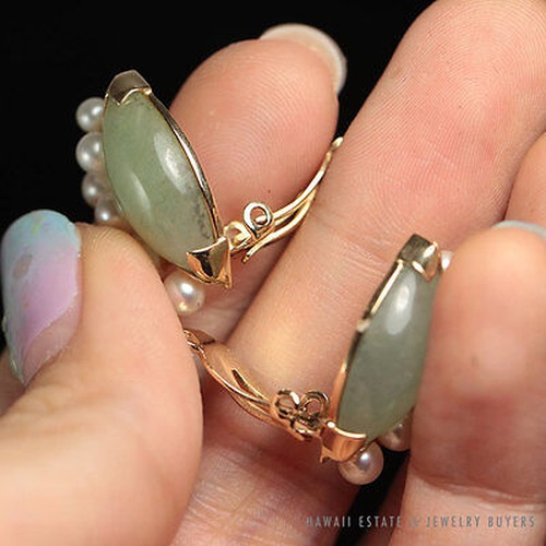 Jade and pearl earrings held in a hand to show their curved gold frames.