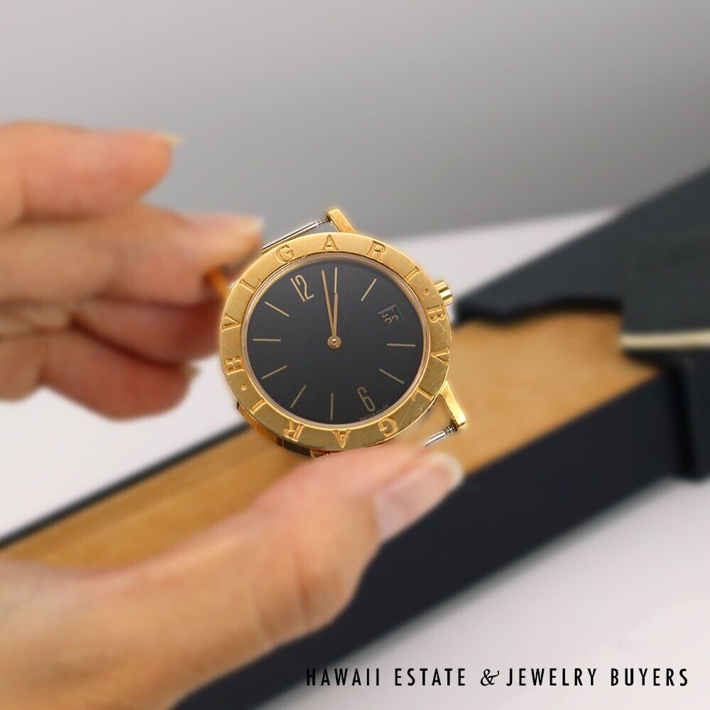 Bvlgari watch body held in front of its box, showing the black dial and gold bezel.