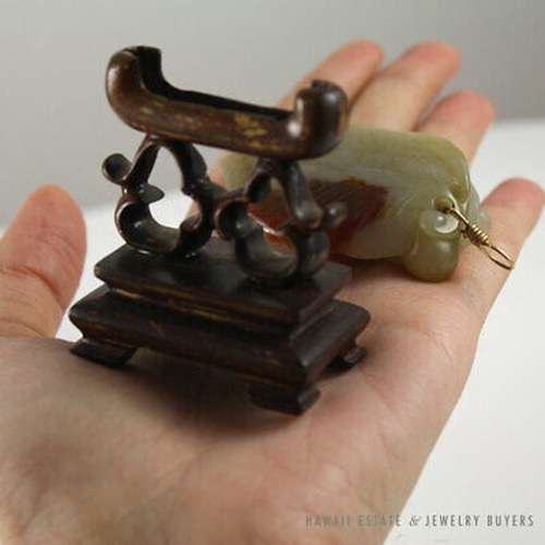 Pendant and openwork wooden stand resting in a palm.
