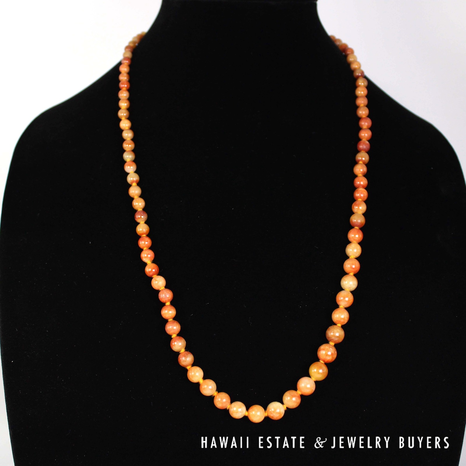 Graduated red-orange jade necklace on a black display bust.