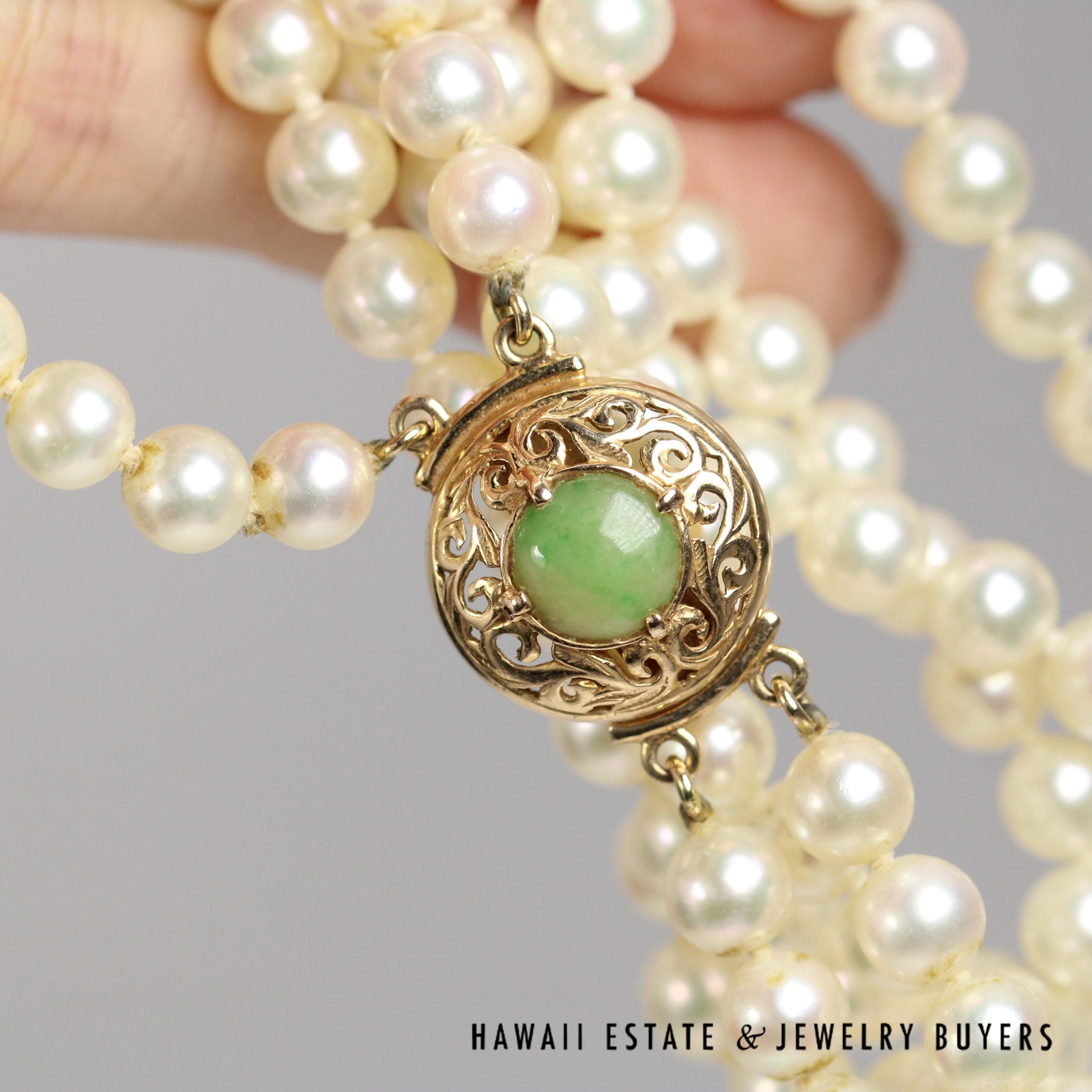 Jade clasp held in a hand beside the pearl strands.