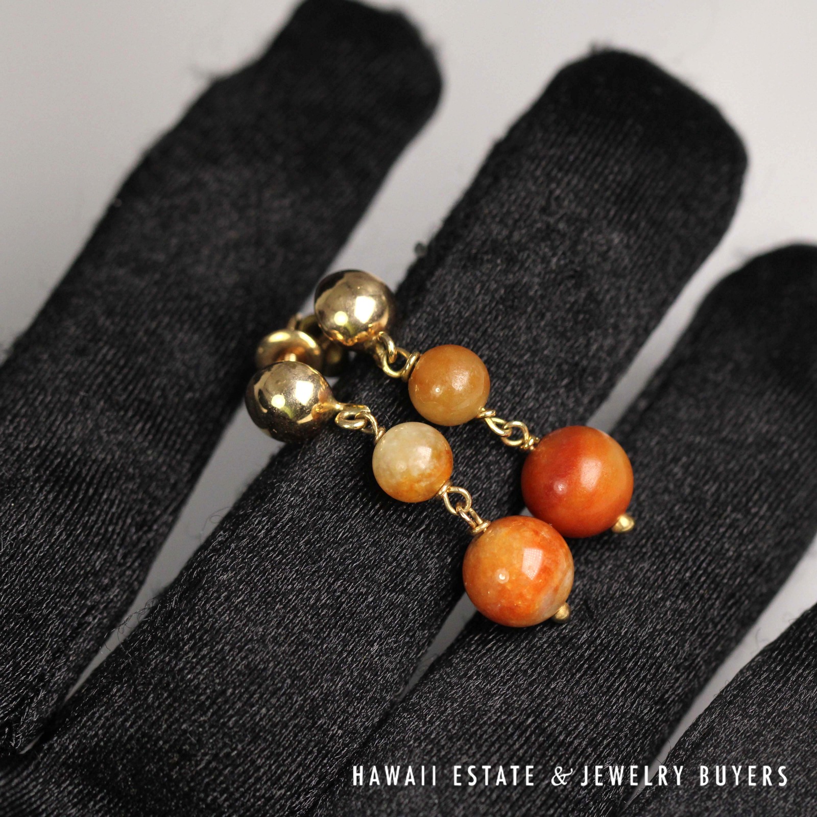 Front view of the paired bead-drop earrings on a black glove.