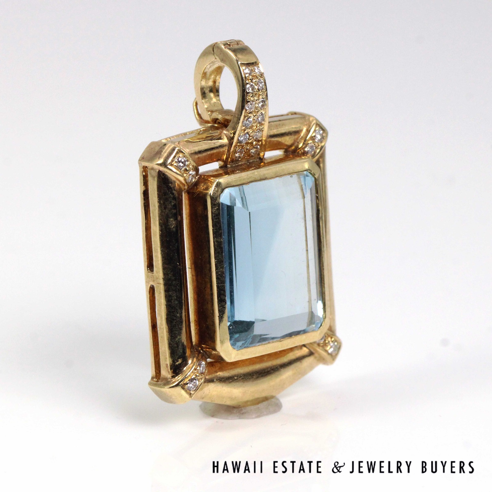 Angled view showing the blue topaz, diamond-set bail and open spaces in the gold frame.