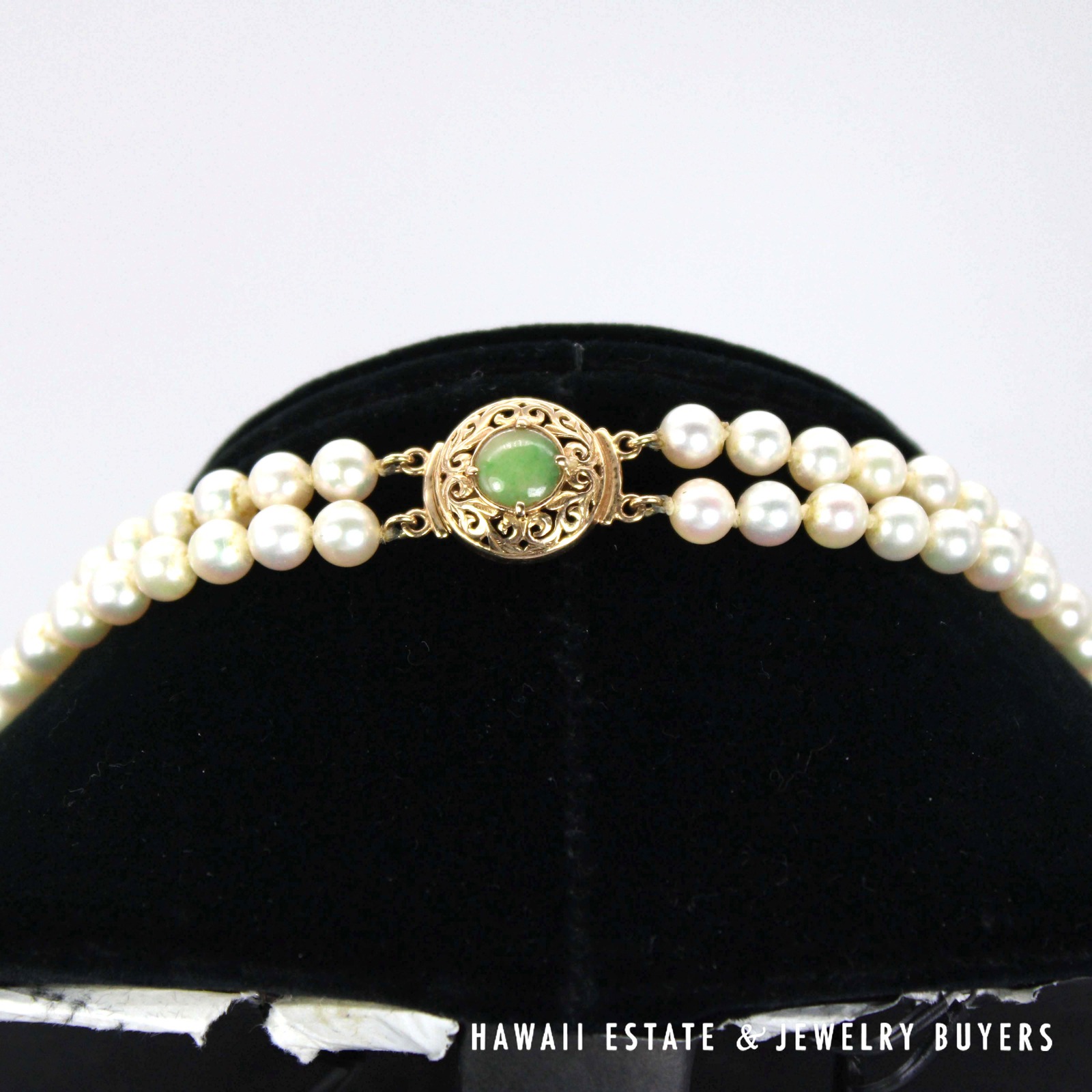 Green jade scroll clasp positioned above the two pearl strands on a display.