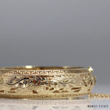 Po Sun Hon yellow gold bangle showing cranes, foliage and geometric borders, with the safety chain extending to the right.