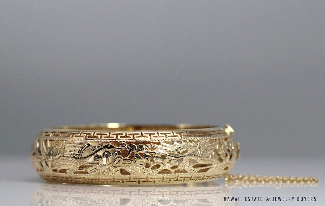 Po Sun Hon yellow gold bangle showing cranes, foliage and geometric borders, with the safety chain extending to the right.