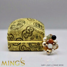Multicolor stone and pearl cluster ring beside its patterned presentation box.