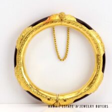 Black coral and yellow gold bangle standing upright, showing its patterned borders, smooth inner surface and connecting chain.