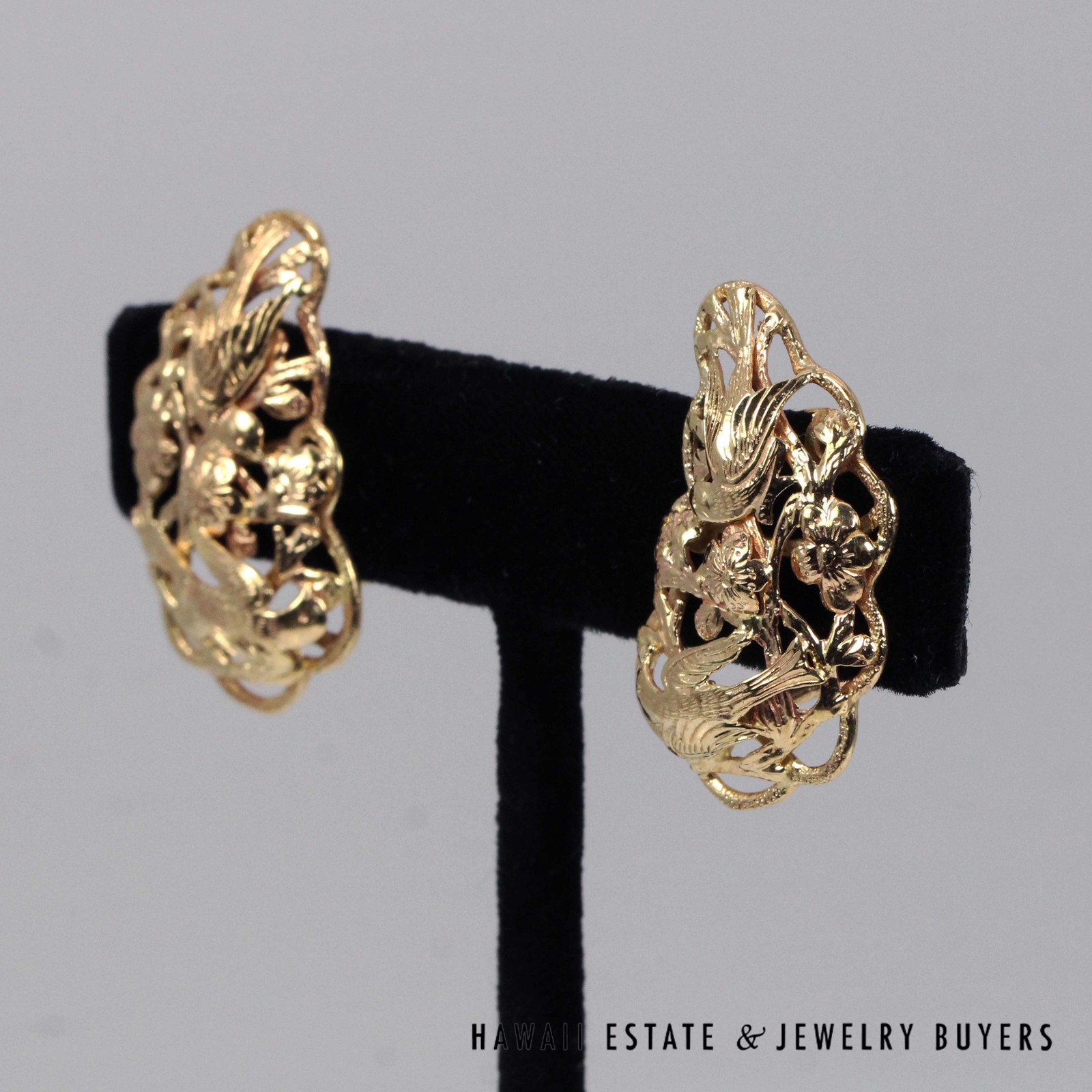 Angled view of the Bird in Plum earrings showing raised birds and blossoms within curved borders.