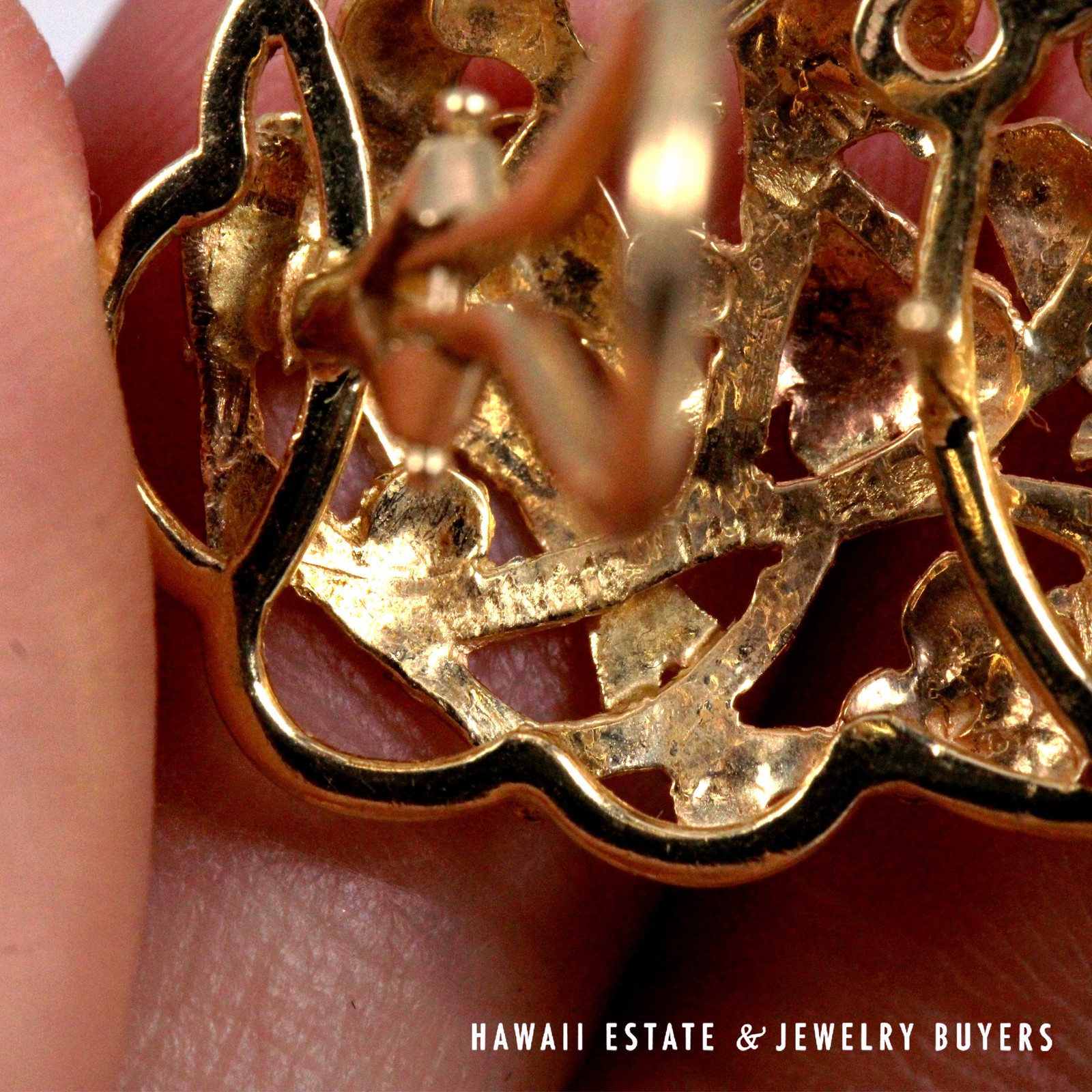 Close-up of the back of an elongated gold earring, showing its clip assembly and stamped markings.