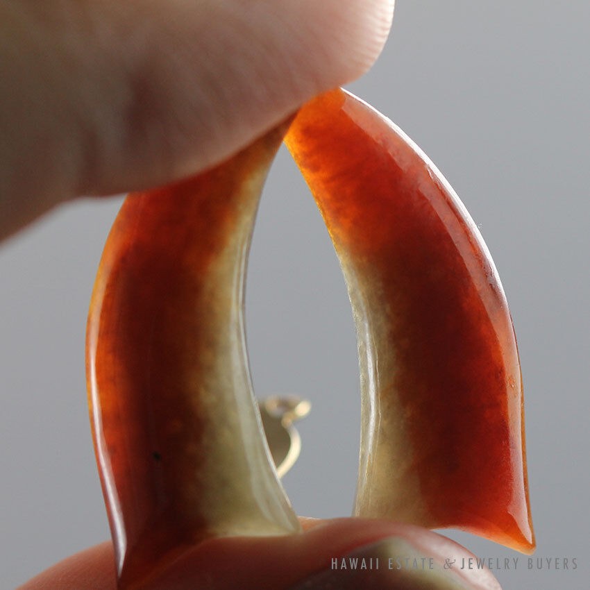 Curved earrings held against the light, showing their contrasting color areas.