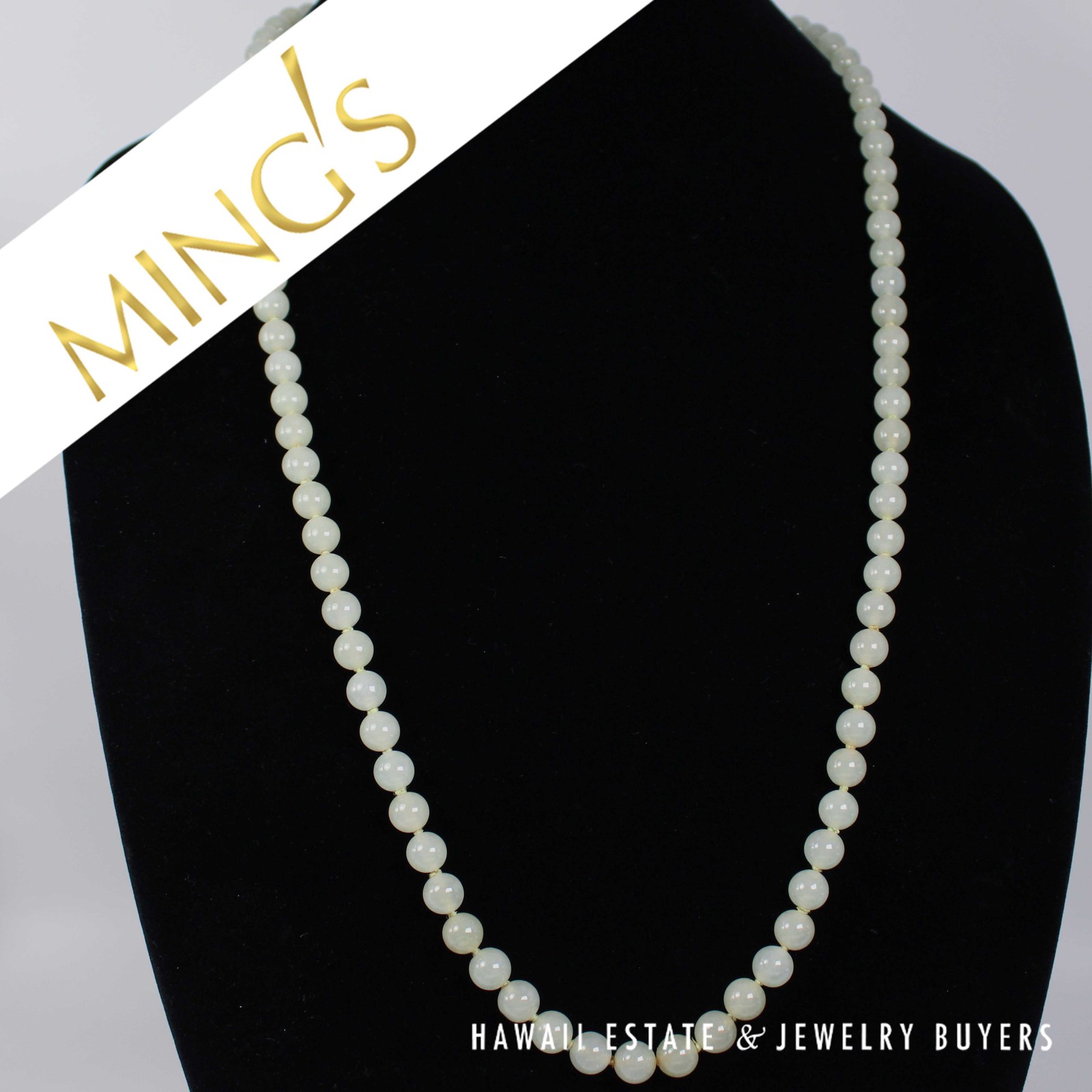 Ming's pale green jade bead necklace displayed on a black bust.