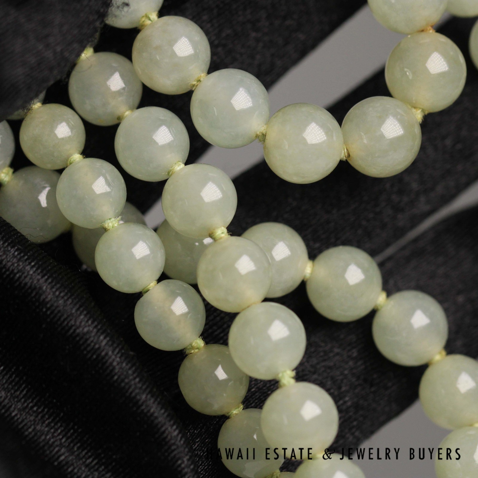 Close view of the rounded pale green jade beads against a black glove.