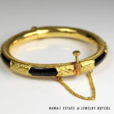 Black plastic bangle with gold sheathing, showing the raised screw closure and attached chain.