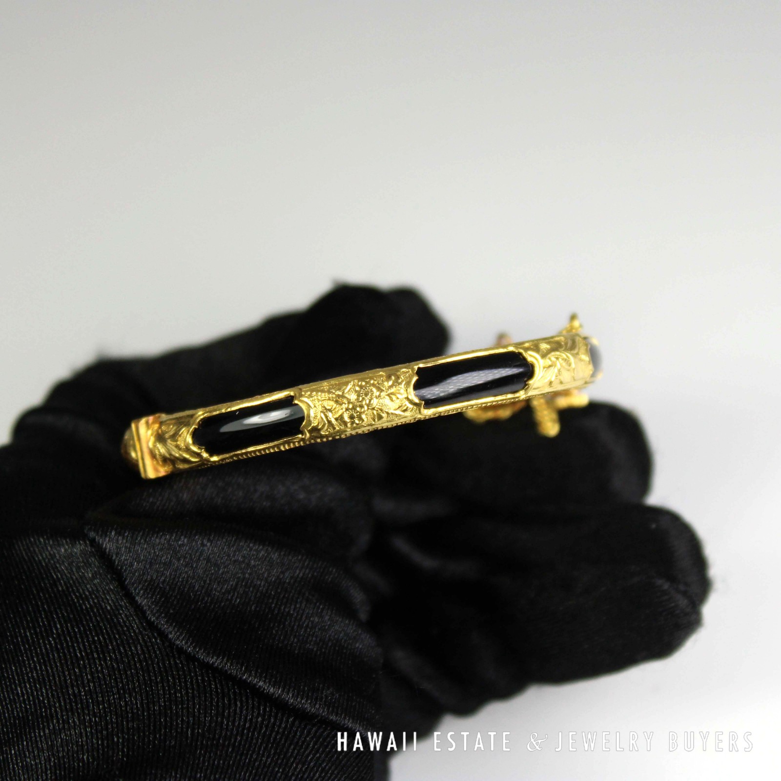 Side view held in a gloved hand, showing alternating black sections and floral gold decoration.
