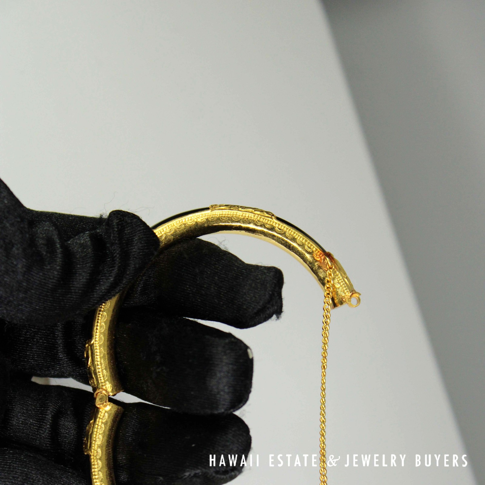 Open bangle held in a gloved hand, showing the inner edge, hinge and hanging chain.